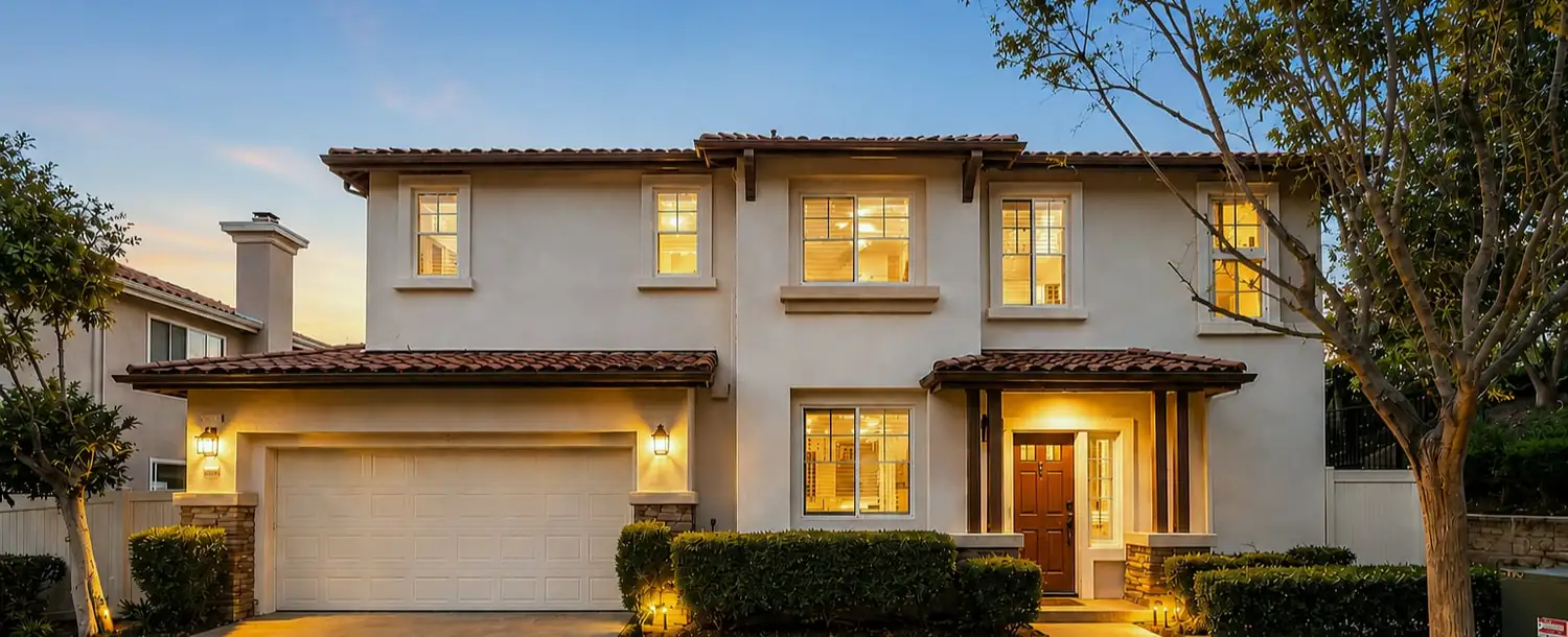 Twilight exterior of a stucco home with warm interior lighting